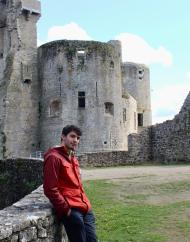A student poses in front of ruins of an old, stone building on a sunny day.