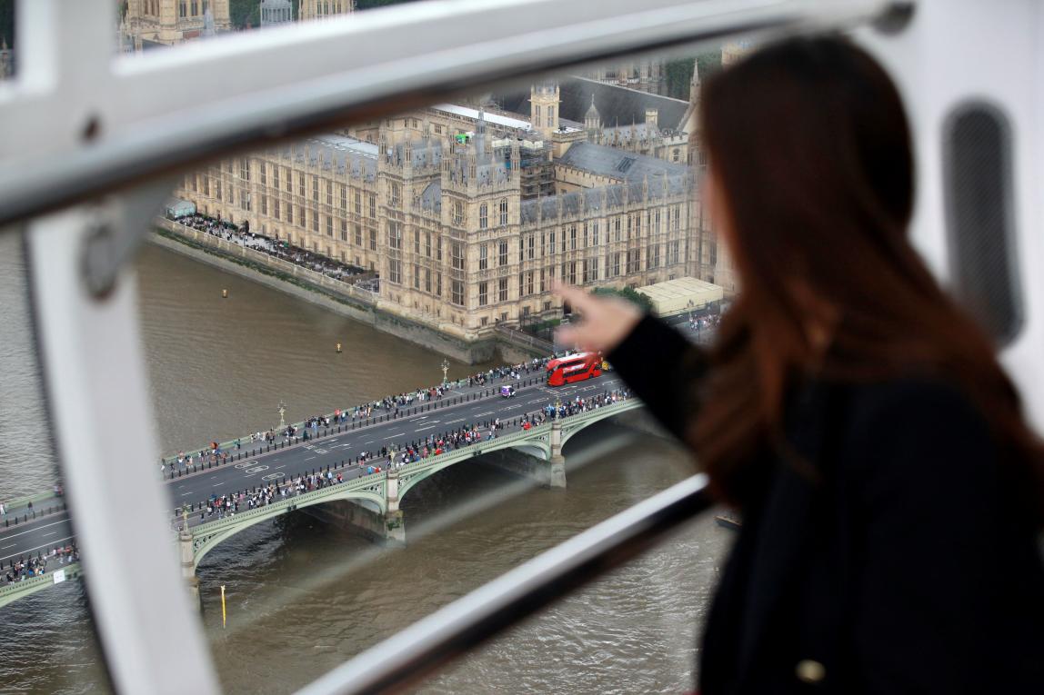 student sitting in front of glass pointing at scene below of bridge, water, and big ben building in london