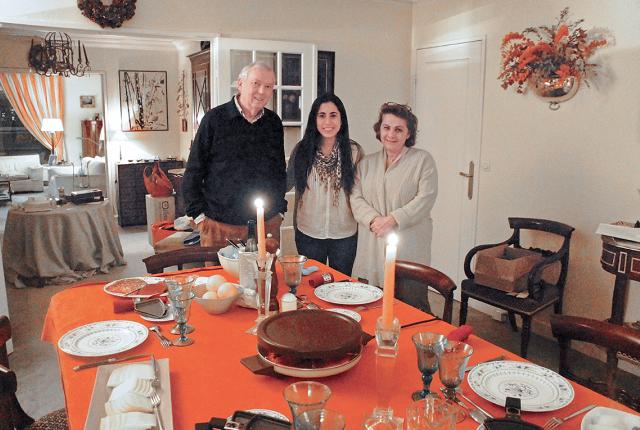 A student with their host parents standing at a set dining room table in a Paris homestay.