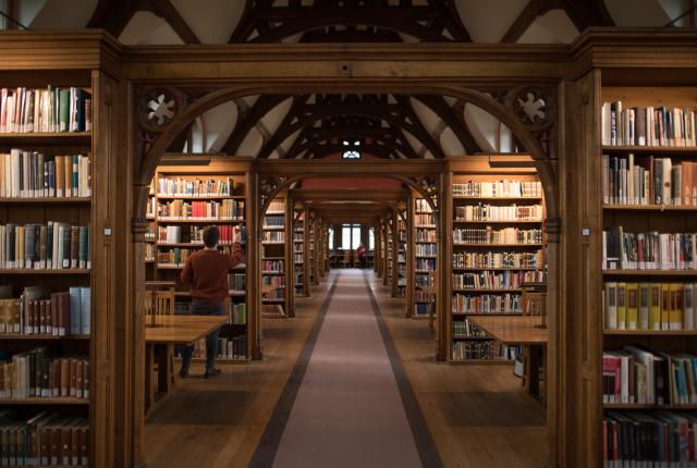 wooded library with walls of books and a long carpet hallway