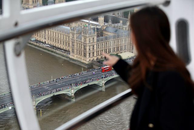 student sitting in front of glass pointing at scene below of bridge, water, and big ben building in london