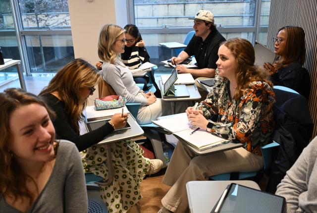 几名学生开心地围坐在一起，有的把课桌转过来面对同学，正热烈讨论着。