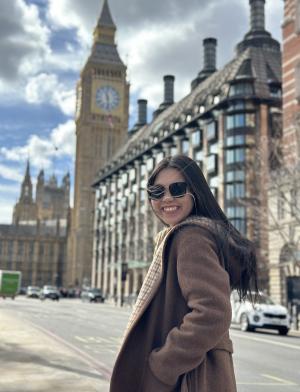 student in jacket and sunglasses walking down a sunny sidewalk towards big ben