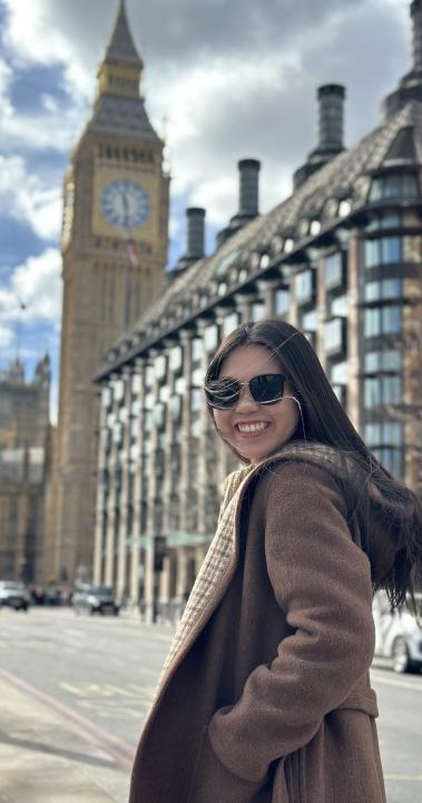 student in jacket and sunglasses walking down a sunny sidewalk towards big ben